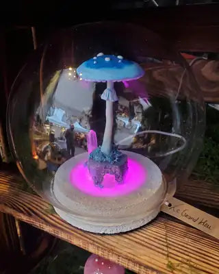 Cloche en verre avec un grand champignon bleu à pois blancs et des cristaux, socle lumineux